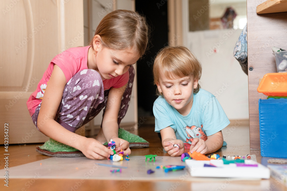 Russia, Moscow, October 2020 - two little happy kids a boy of four year old and a girl of seven year old siblings or friends at home on floor together playing and sculpting with plasticine Russia, Moscow, October 2020 - two little happy kids a boy of four year old and a girl of seven year old siblings or friends at home on floor together playing and sculpting with plasticine
