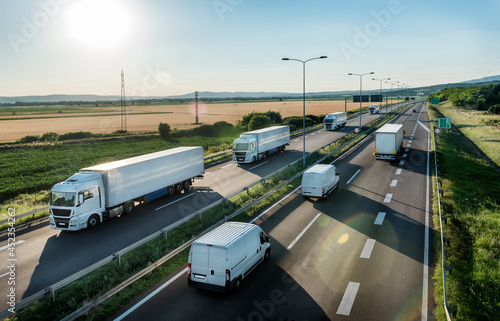Obraz na plátně Convoy or caravans of transportation trucks passing vans and truck on a highway on a bright blue day