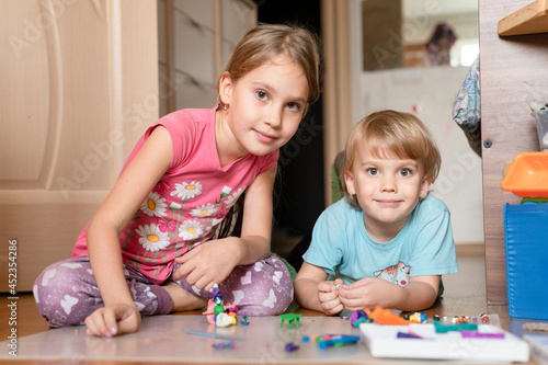Russia  Moscow  October 2020 - two little happy kids a boy of four year old and a girl of seven year old siblings or friends at home on floor together playing and sculpting with plasticine