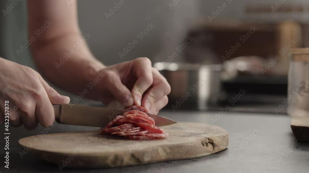 Slow motion man slicing salami on olive board Slow motion man slicing salami on olive board