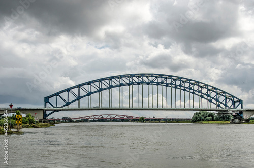 Zwolle, the Netherlands, August 10, 2021: view along the IJssel river with the historic arch bridge and beyound it the new Hanzeboog bridge, under a dramatic sky © Frans