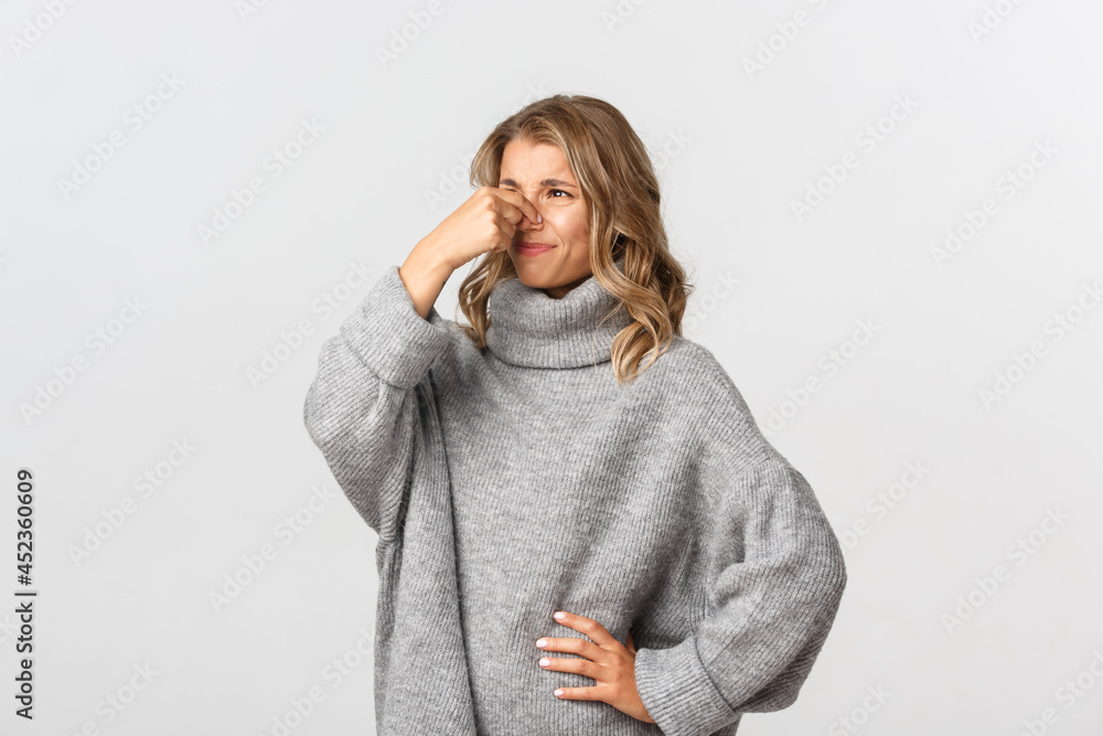 Portrait of disgusted blond girl shut her nose and grimacing from bad