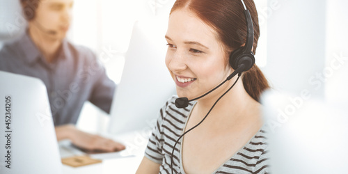 Konstfotografi Casual dressed young woman using headset and computer while talking with customers online