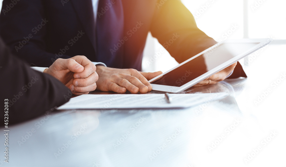Business people using tablet computer while working together in sunny modern office. Unknown businessman with colleague at workplace. Teamwork and partnership concept Business people using tablet computer while working together in sunny modern office. Unknown businessman with colleague at workplace. Teamwork and partnership concept