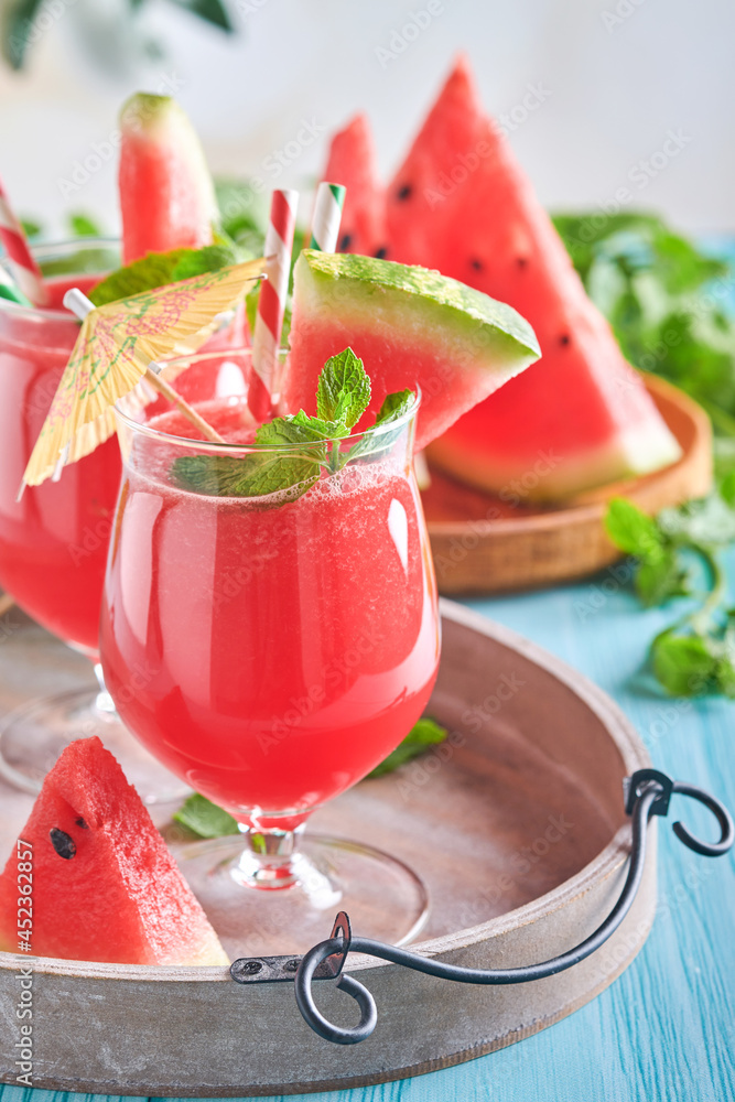 Watermelon cocktail with mint and ice. Summer refreshing drinks in glasses on blue wooden table. Concept of healthy summer eating.