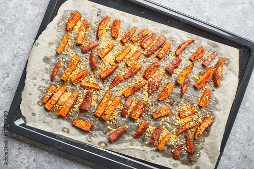 Sweet potatoes with cheese baked on baking sheet on gray background.