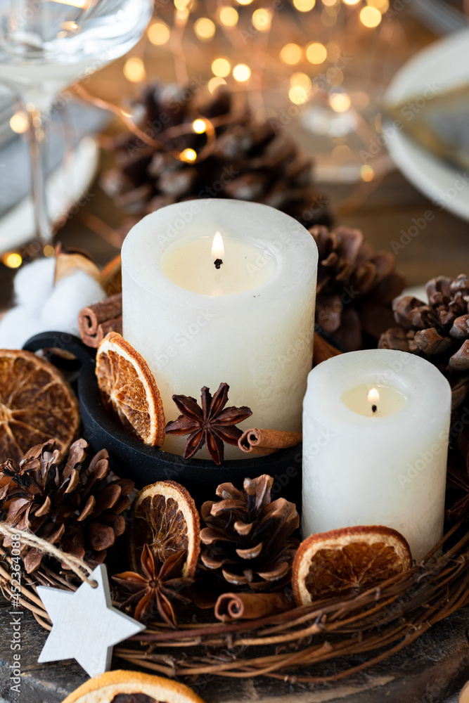 Rustic decor for christmas holiday family dinner. Center piece with white candle, dry orange, cones, cotton. Zero waste eco friendly home decoration. Cozy atmosphere, wooden background. Close up Rustic decor for christmas holiday family dinner. Center piece with white candle, dry orange, cones, cotton. Zero waste eco friendly home decoration. Cozy atmosphere, wooden background. Close up