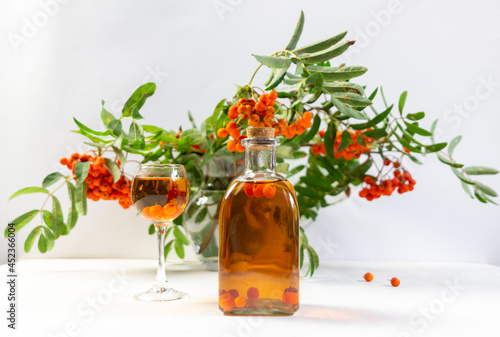 rowan berry tincture in glass and bottle with rowanberry branhes bouquet in vase on white background