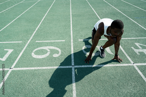 An African American male track and field athlete in sportswear stands at a low start before the race at the stadium