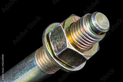 Hexagonal nut and washer on metal galvanized anchor bolt end on black background. Artistic detail of thread on anchoring rod into concrete with yellow chromate conversion coating to protect corrosion.