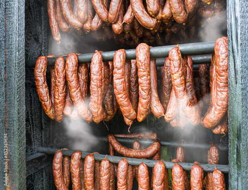Smoking of spicy kielbasa salamis in a wooden smoke house detail. Closeup of hot smoky sausages from pork and beef meat hanging inside homemade smokery. Making tasty savoury charcuterie in smokehouse. photo
