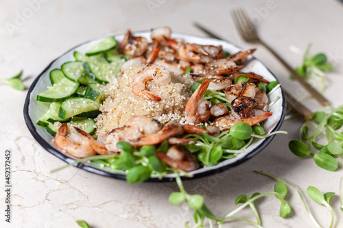 Quinoa with grilled prawns or shrimps, cucumber and micro greens on the marble background side view.