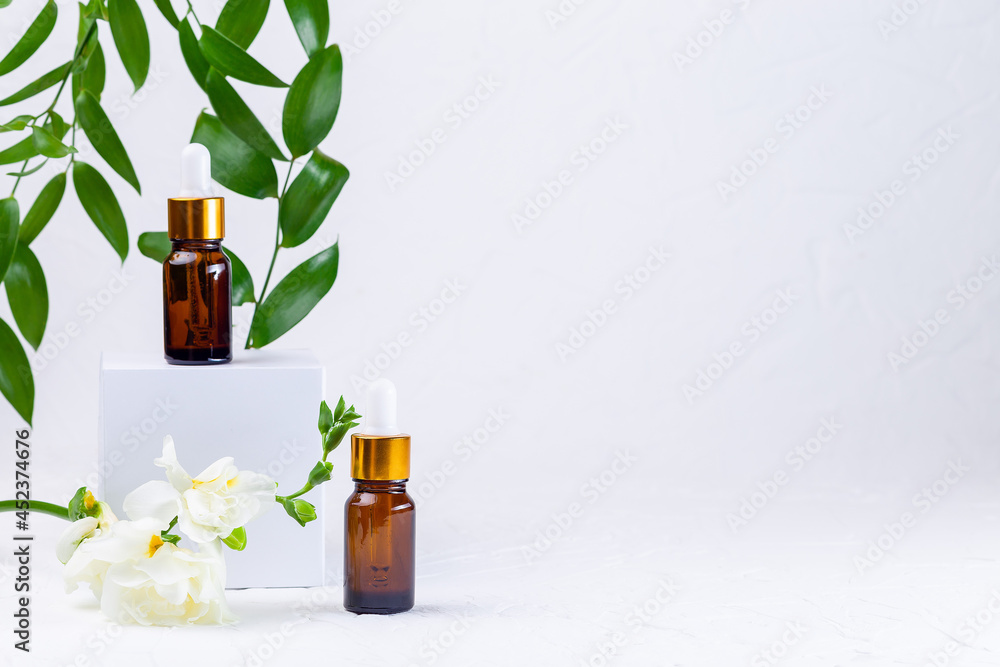 Brown glass pipette bottles with white podium, flowers and green leaves Brown glass pipette bottles with white podium, flowers and green leaves