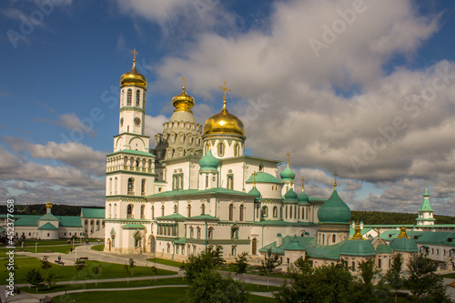 beautiful architectural ensemble of white stone churches with golden domes in New Jerusalem on a sunny summer day against a bright blue sky with clouds in Istra Moscow region