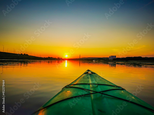 View of front of kayak, floating on the river at summer sunset