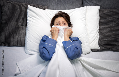 Cuadro en lienzo Worried woman with nightmares lying in bed and covering face with blanket