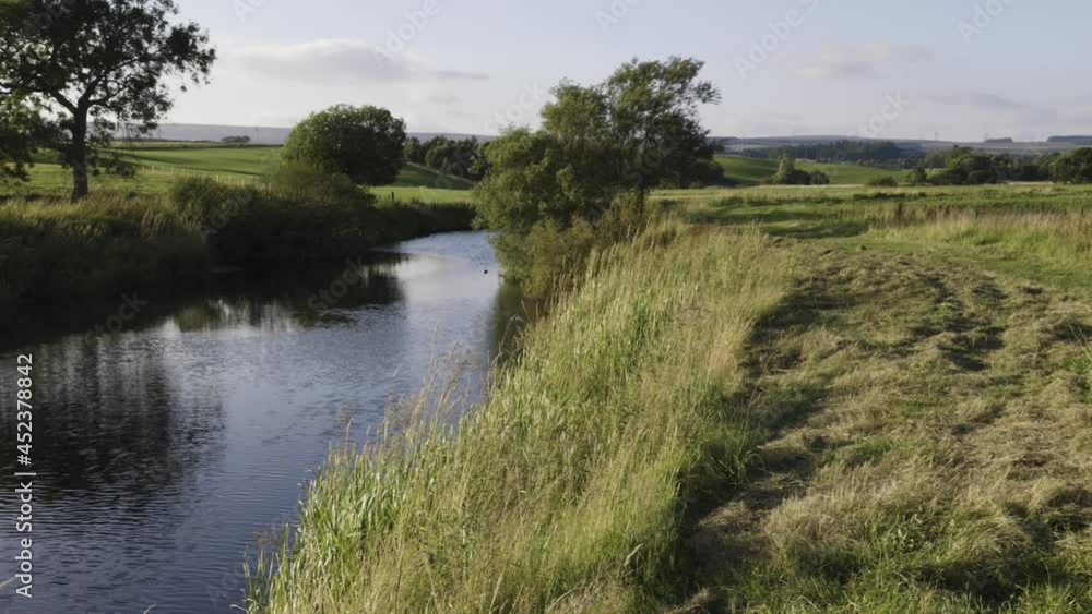 Calm river flowing through green fields in the countryside on a warm, summers day.