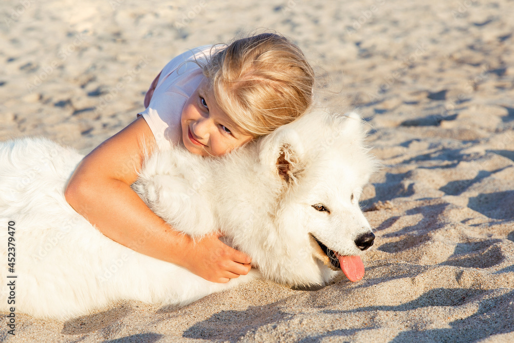 A dog is a child's friend. A preschool-age girl hugs a dog, a white Samoyed husky on the seashore. Pets, the concept of trust and friendship with animals.
A dog is a child's friend. A preschool-age girl hugs a dog, a white Samoyed husky on the seashore. Pets, the concept of trust and friendship with animals.
