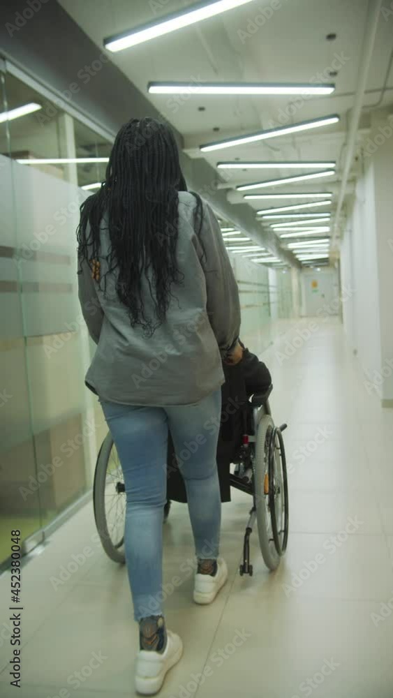 A young lady is driving her colleague in a wheelchair through the office