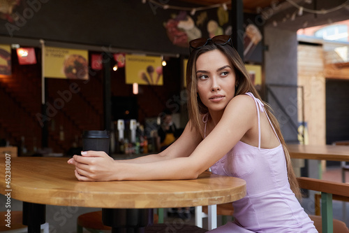 beautiful young asian woman with dark long hair in light pink dress sitting at table of dinery, having rest. pretty student lady having cup of coffee at cafe veranda. summer chill, rest, lifestyle