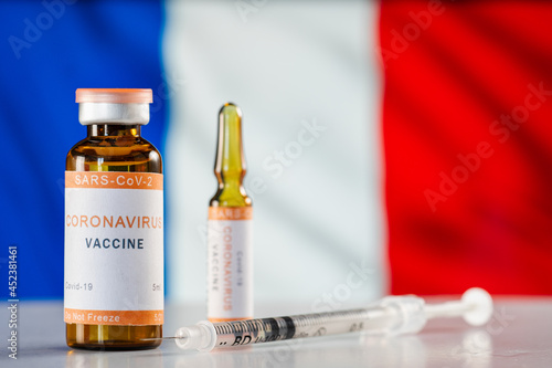 A vaccine against the COVID-19 coronavirus and a medical syringe on background of French flag. The concept of treatment, immunization and vaccination in case of a pandemic in France.