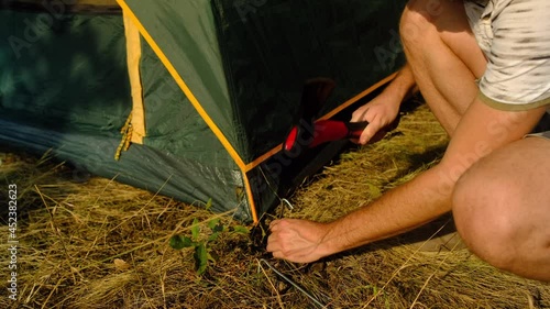 Man with beard sets up a tent in tourist camp. Female hammers peg with an axe. photo