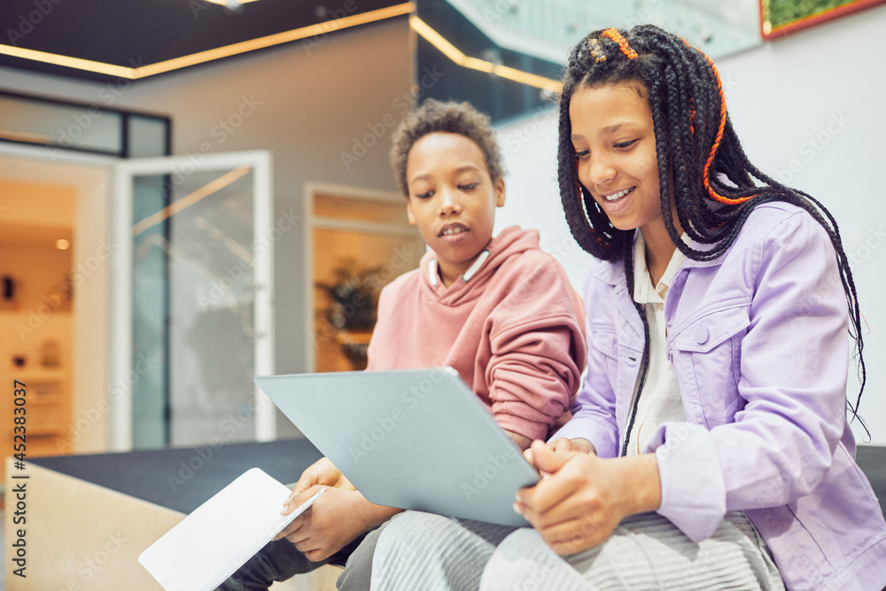 Portrait of two African-American schoolkids using laptop in modern school interior, copy space Portrait of two African-American schoolkids using laptop in modern school interior, copy space