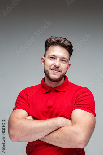 Smiling young confident handsome man with beard and arms crossed on gray studio background. Positive person