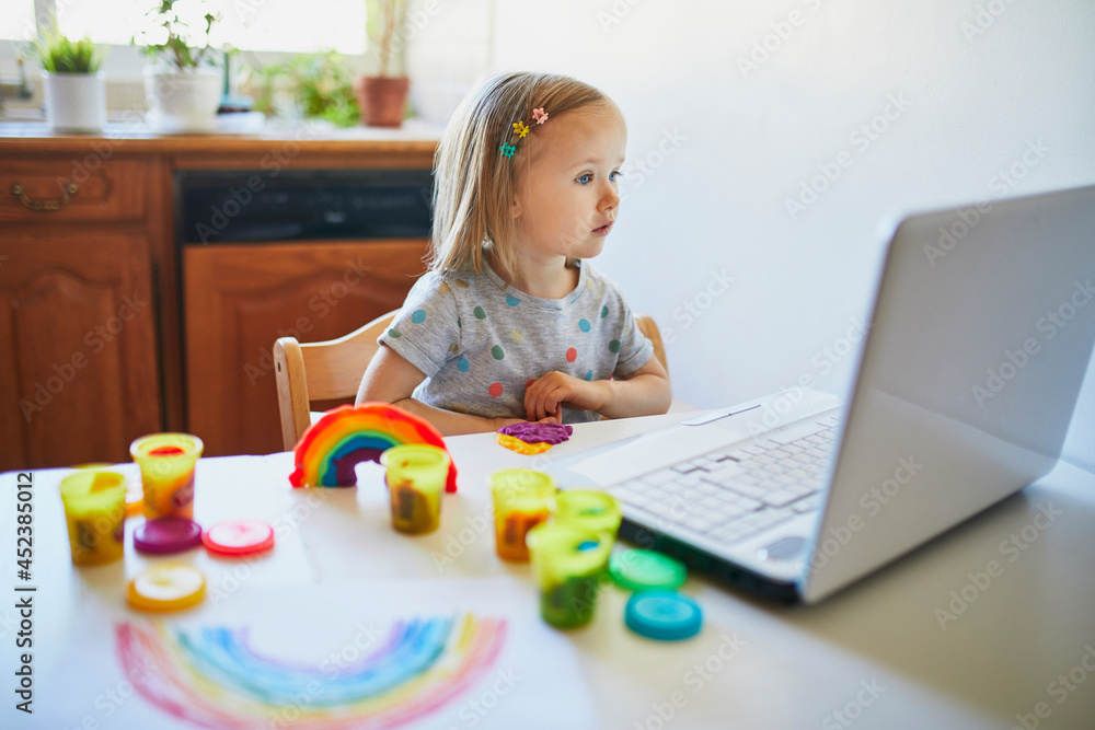 Toddler girl playing modelling clay in front of laptop Toddler girl playing modelling clay in front of laptop