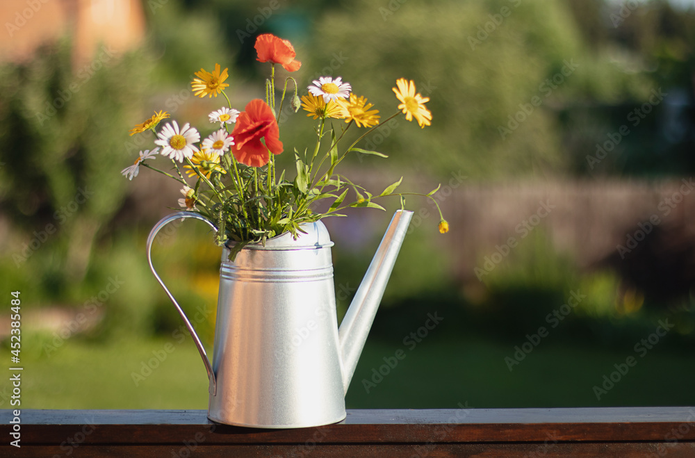 Fototapeta premium A bouquet of red poppies and daisies in a metal watering can. Summer floral background. Copy space