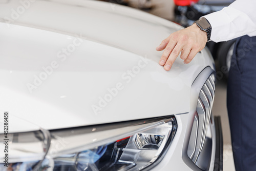 Close up man male hand customer buyer client wearing white shirt chooses auto wants to buy new automobile touch glossy hood in showroom vehicle salon dealership store motor show indoor Sales concept.
