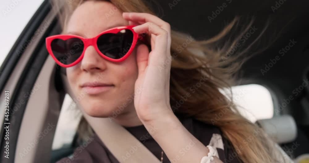 Young happy woman with heart shaped sunglasses making selfie video in car during road trip, goofing around. Customer generated video content. Young happy woman with heart shaped sunglasses making selfie video in car during road trip, goofing around. Customer generated video content.