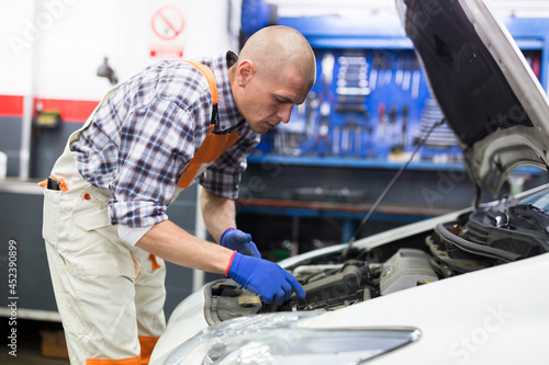Professional mechanic man in uniform repairing car by customer claim order in auto repair shop garage