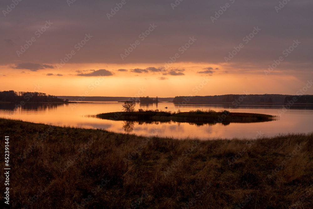 Small island with single tree, in autumn, at sunset. Absolutely smooth water surface. Boat floats in distance. Spectacular silhouettes and bright colors Small island with single tree, in autumn, at sunset. Absolutely smooth water surface. Boat floats in distance. Spectacular silhouettes and bright colors
