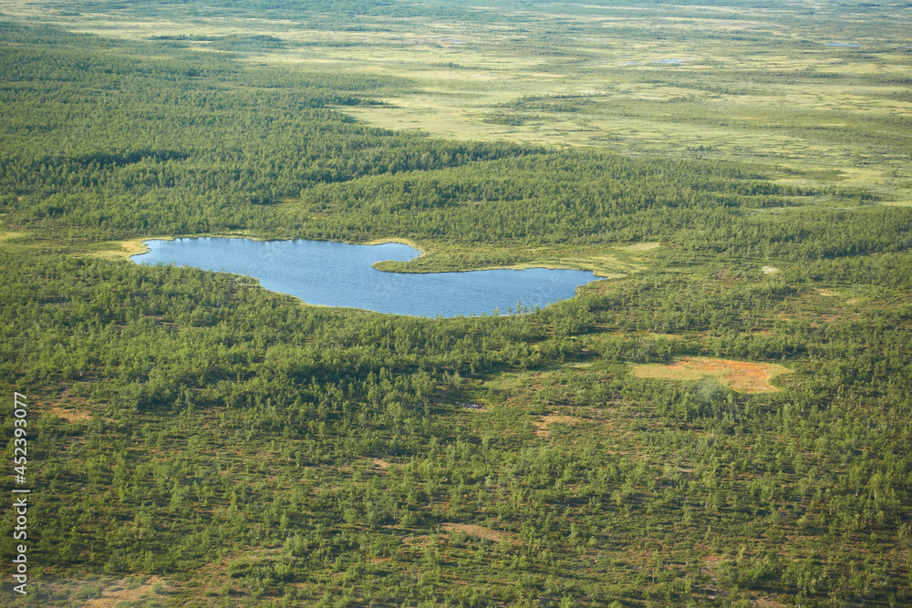 Aeriel view to Kiruna wilderness from helicopter with small lake or pond in the middle of the swamps and trees in far north of Swedish Lapland.
