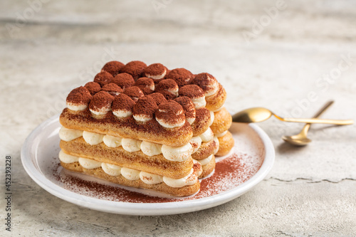 Tiramisu on a white plate. Italian dessert made of ladyfingers dipped in coffee and layred with cream made of eggs and mascarpone cheese, powdered with cocoa.