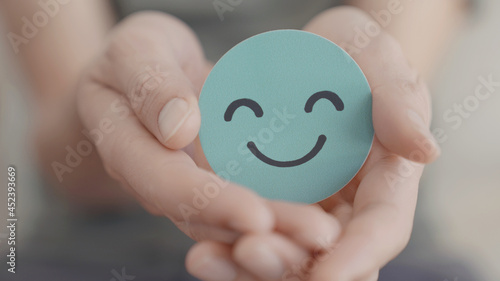 Hand holding green happy smile face paper cut, mental health assessment, child positive wellness, world mental health day, compliment  day, mindful concept photo