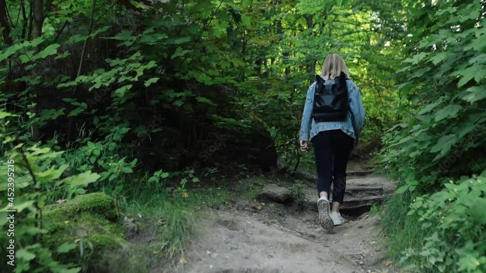 Young beautiful girl walks through the woods in a denim jacket and with a backpack. Beautiful background. Relax alone. Self-isolation in nature, young student walking in the woods. High quality 4k Young beautiful girl walks through the woods in a denim jacket and with a backpack. Beautiful background. Relax alone. Self-isolation in nature, young student walking in the woods. High quality 4k