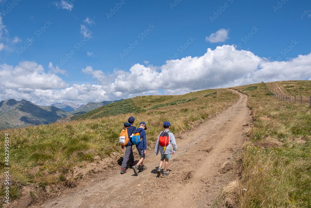 three children with backpacks on their backs are hiking along a mountaintop path