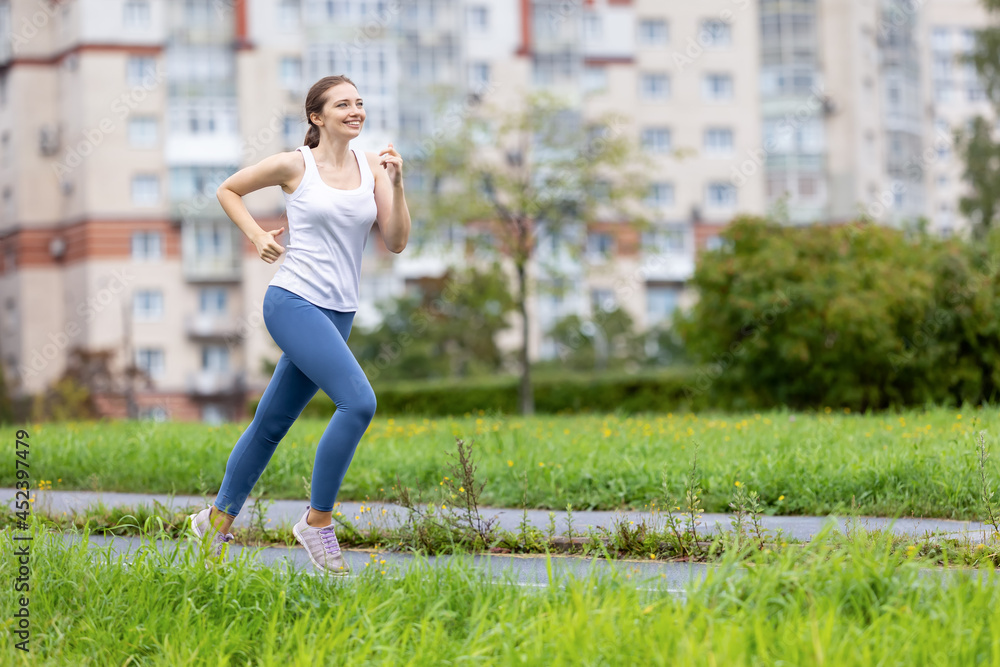 Smiling woman in leggins runs in public park in morning.