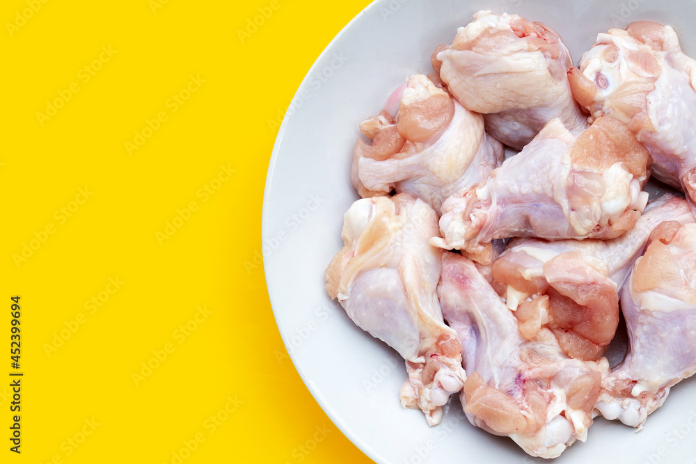 Fresh raw chicken wings (wingstick) in white plate on yellow background.