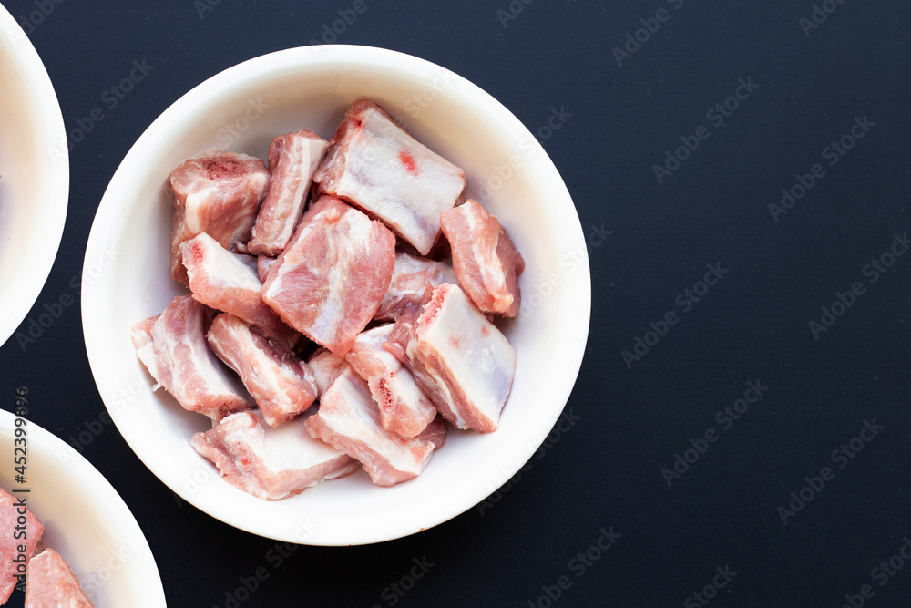 Raw pork ribs in white bowl on dark background