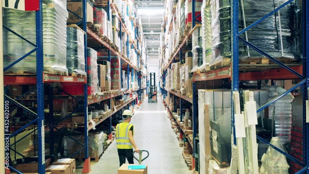 Warehouse passage with a male employee pulling a trolley Warehouse passage with a male employee pulling a trolley