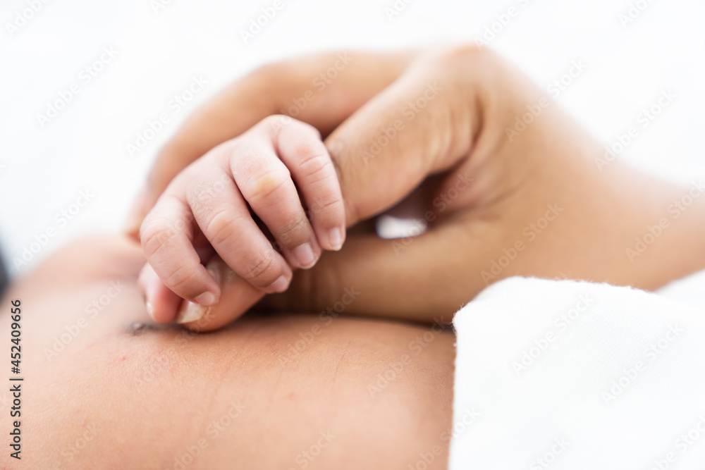 Newborn baby holding mother’s finder while sleeping on white bed. Mother takes care and comforting for her baby Newborn baby holding mother’s finder while sleeping on white bed. Mother takes care and comforting for her baby