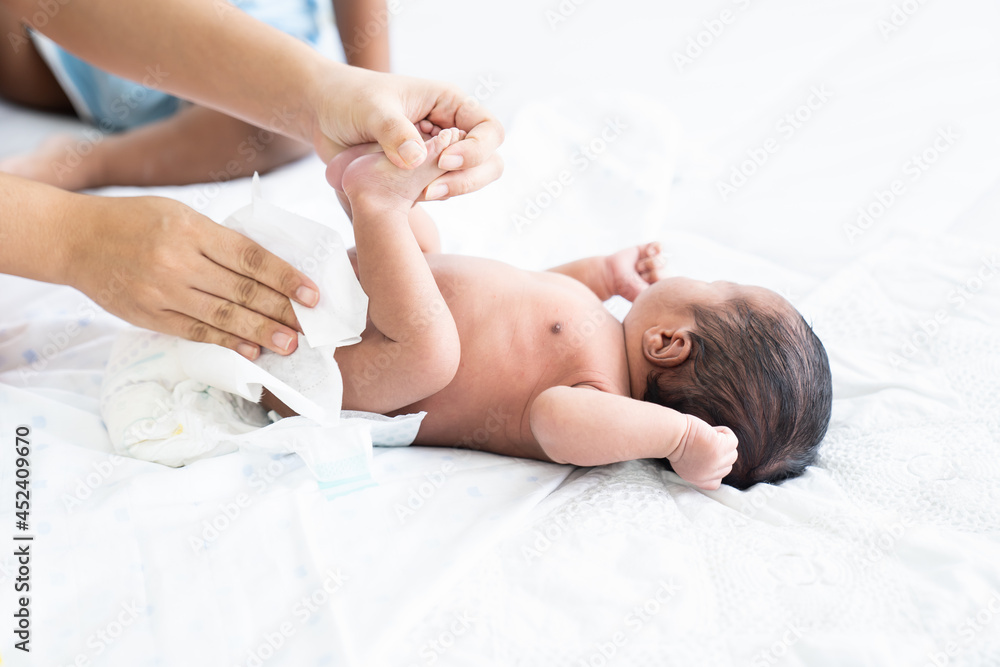 Mom wiping her newborn baby skin, face with wet wipes carefully on bed at home. family, cleaning wipe and infant concept