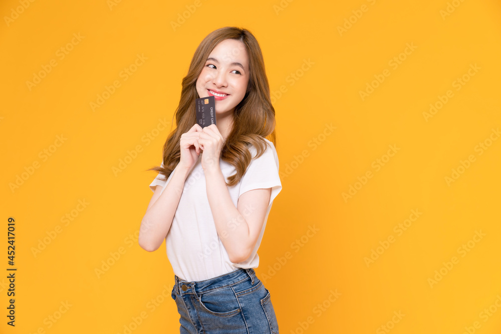 Cheerful beautiful Asian woman in white t-shirt and holding mockup credit card on yellow background. Cheerful beautiful Asian woman in white t-shirt and holding mockup credit card on yellow background.