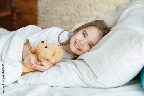 baby lying in bed with Taddy Bear. Little girl sleeps with knitted toy