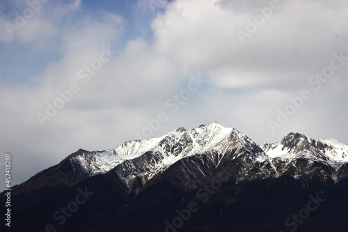a dark mountain range with snow-capped peaks against a background of white clouds