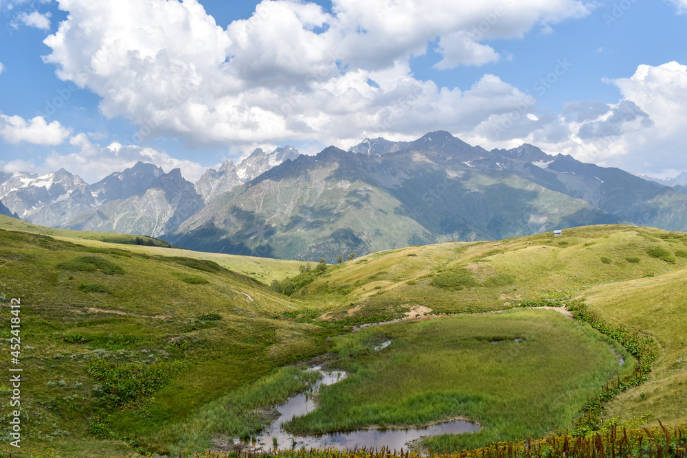 Obraz premium Summer mountain landscape in Svaneti region, Georgia, Asia. Snowcapped mountains in the background. Blue sky with clouds above. Georgian travel destination