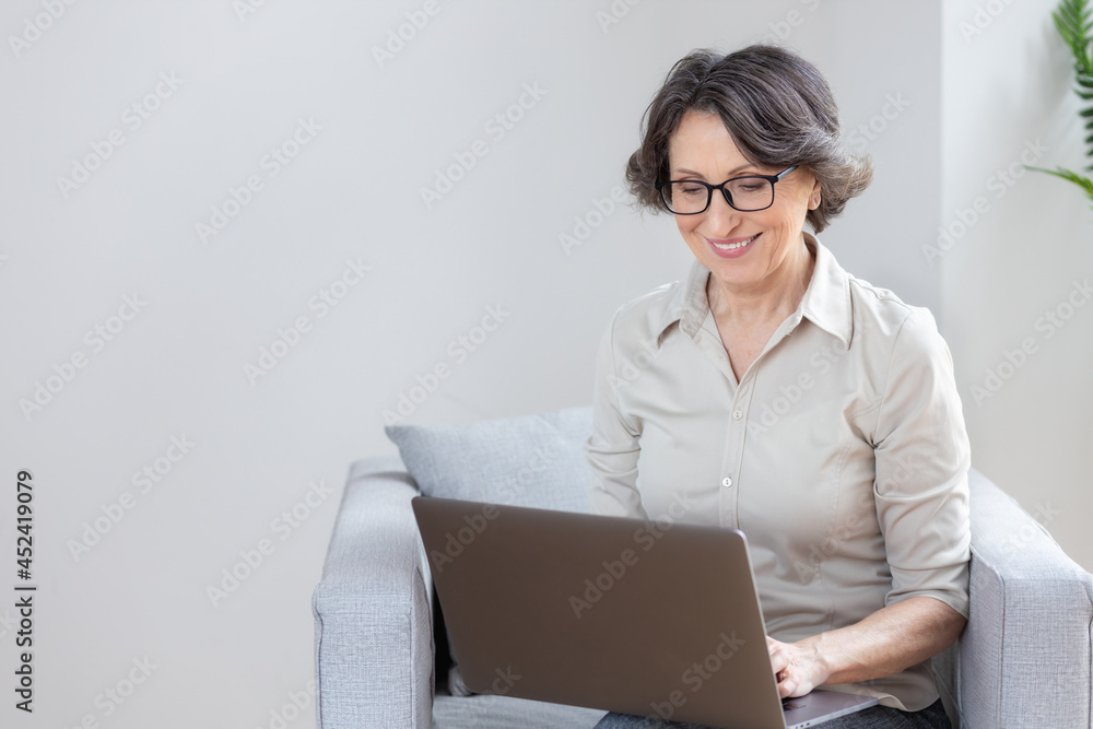 Video call, remote work concept. Beautiful caucasian aged business woman using laptop computer for online communication via the internet sitting on an armchair in the office or at home Video call, remote work concept. Beautiful caucasian aged business woman using laptop computer for online communication via the internet sitting on an armchair in the office or at home